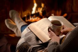 54094172 – woman resting with cup of hot drink and book near fireplace alternate text for this image