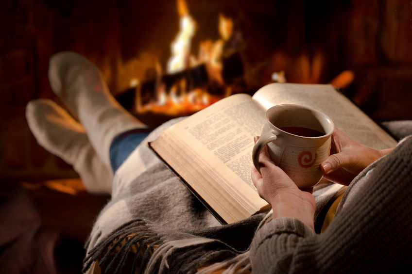 54094172 – woman resting with cup of hot drink and book near fireplace alternate text for this image