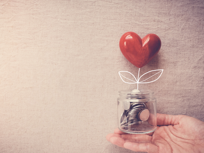Hand holding a jar of heart tree growing on money coins, social responsibility and donation concept alternate text for this image