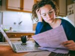 Young brunette curly female reading her bill papers, looking stressed