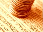 "A stack of pennies on a financial newspaper with stock quotes. Shallow DOF, gold-toned."